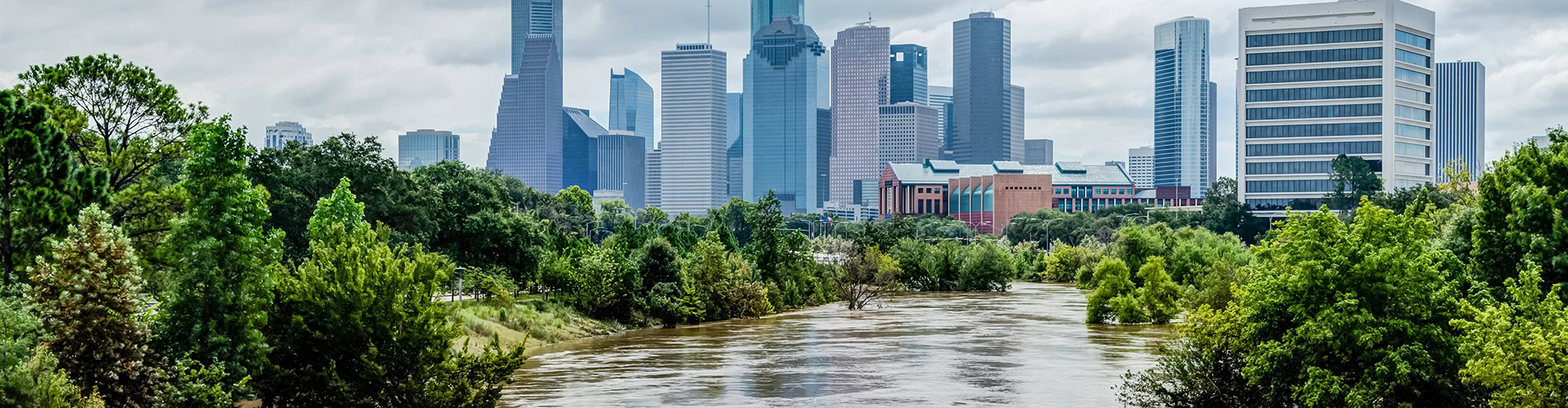 High And Fast Water Rising In Bayou River With City in Background